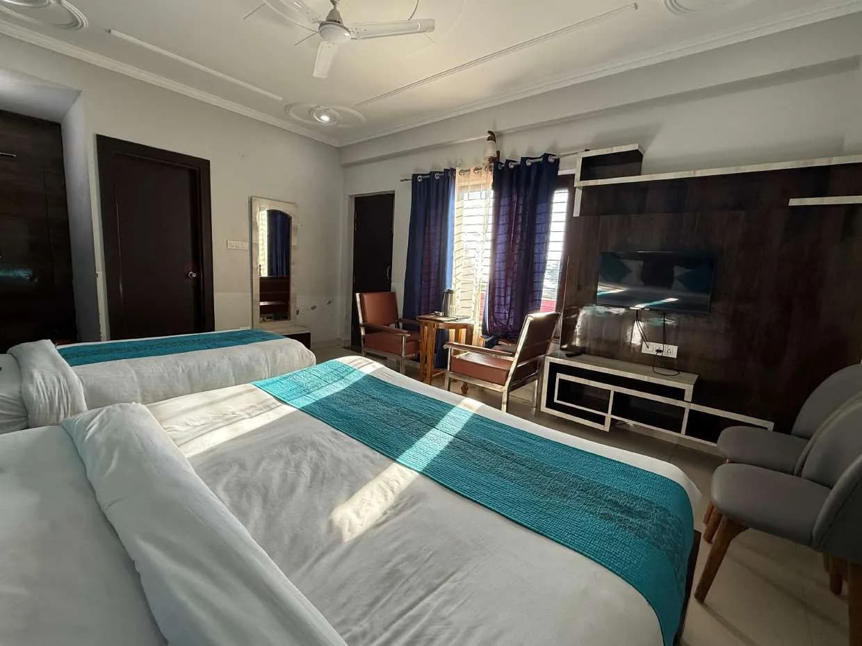 Room view showing two beds, TV unit, mirror and window curtains